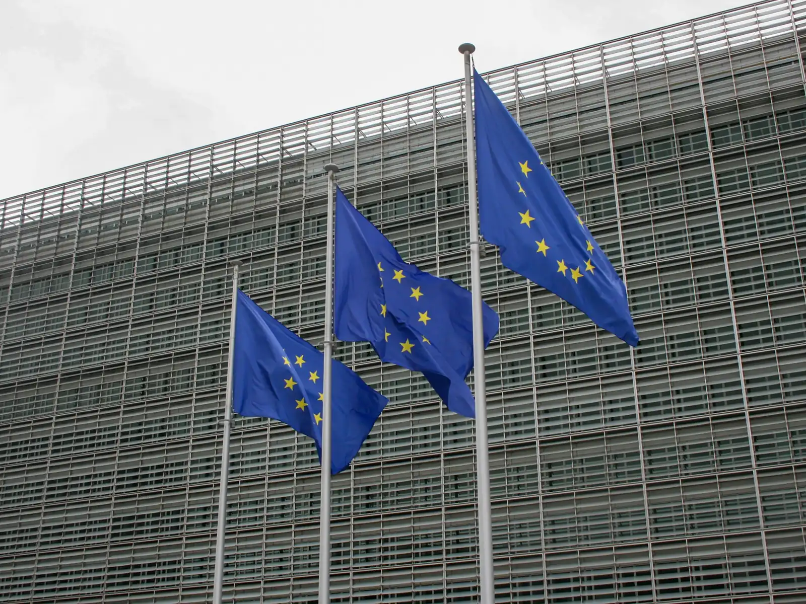 Drei Europaflaggen wehen vor der Rasterfassade eines EU-Verwaltungsgebäudes in Brüssel